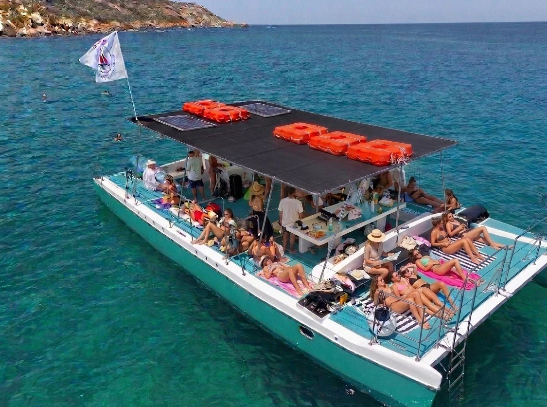 Großer privater Katamaran vor Anker im türkisblauen Wasser von Comino, eine Gruppe beim Sonnenbaden