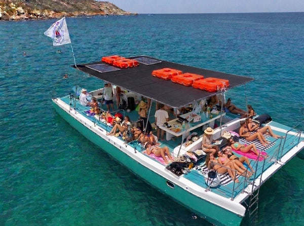 Large private catamaran with a group sunbathing, at anchor in the turquoise water of Comino