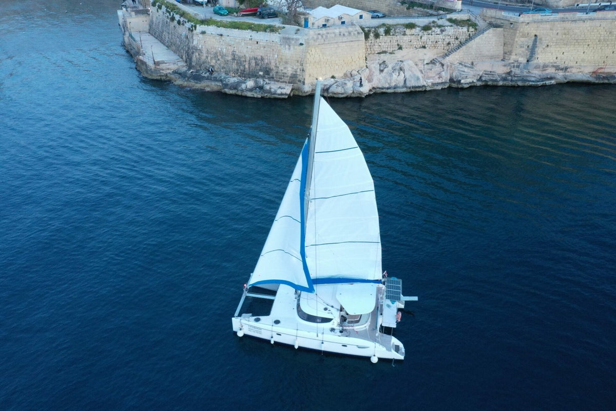 Catamarano a vela a vele spiegate davanti ai bastioni di La Valletta