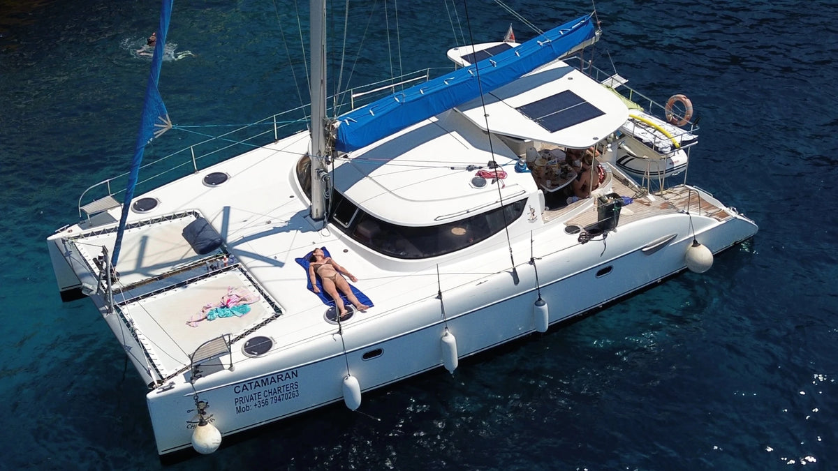 Catamarano a vela all'ancora, una passeggera prende il sole sul ponte